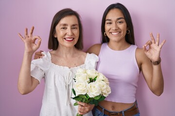 Poster - Hispanic mother and daughter holding bouquet of white flowers smiling positive doing ok sign with hand and fingers. successful expression.