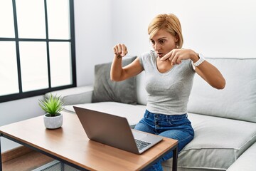 Wall Mural - Middle age blonde woman using laptop at home pointing down with fingers showing advertisement, surprised face and open mouth