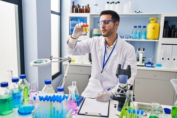 Sticker - Young hispanic man scientist looking urine test tube writing report at laboratory