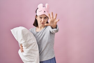 Poster - Woman with down syndrome wearing sleeping mask hugging pillow doing stop gesture with hands palms, angry and frustration expression