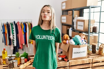 Wall Mural - Asian young woman wearing volunteer t shirt at donations stand looking at the camera blowing a kiss on air being lovely and sexy. love expression.