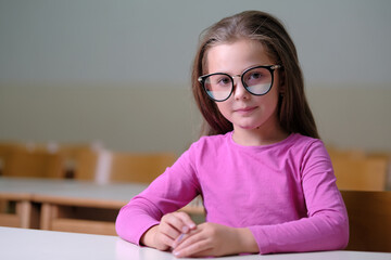 Wall Mural - Portrait of a cute school child girl sitting at a working desk in the classroom.