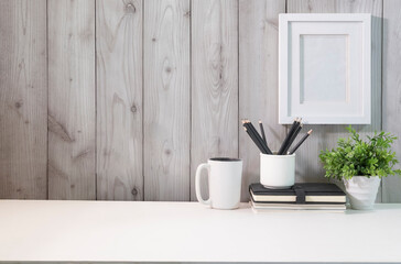 Blank picture frame, pencil holder, notebook and coffee cup on white table.