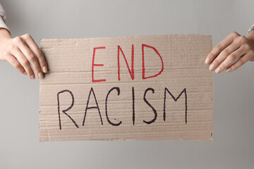 Wall Mural - Hands holding piece of carton with text END RACISM on grey background