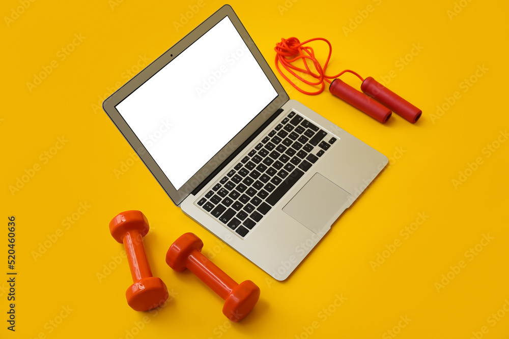 Modern laptop, dumbbells and skipping rope on yellow background