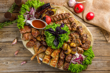 Wall Mural - platter of different kebabs with tomato sauce, greenery on old wooden table top view