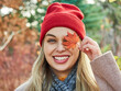 © evafesenuk - Cheerful smiling blonde woman in a red hat closes her eye with a red autumn leaf