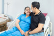 © GAJENDRRA BHATI  - Happy young indian man hugging pregnant wife lying on bed in hospital, Smiling asian couple expecting baby.