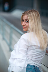 Wall Mural - Beautiful blonde fashionable sexy tourist girl walking in city street with long hair flying in the wind. Woman looking at camera outdoors wearing trendy white t-shirt, denim jean short skirt.