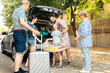 © DC Studio - Happy family travelling at seaside with car, leaving on vacation trip with parents, grandparents and small girl. Loading luggage and suitcase in automobile trunk, summer adventure.