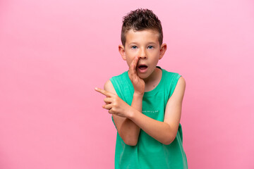 Wall Mural - Little caucasian boy isolated on pink background pointing to the side to present a product and whispering something