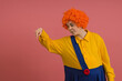 © Sergey - cheerful girl in a clown costume and a bright wig points down on a colored background