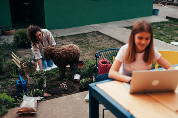 Wall Mural - mother gardening plants in backyard , daughter using laptop