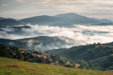 Wall Mural - Amazing view with small mountain huts against the background of beautiful low clouds creeping among the mountain slopes, Rhodopes in Bulgaria at sunrise