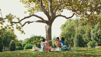 Wall Mural - Happy smiling young multinational people at picnic on summer day outdoors. Friends have fun weekend together, relaxing in the park at picnic