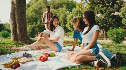 Wall Mural - Happy smiling young multinational people at picnic on summer day outdoors. Friends have fun weekend together, relaxing in the park at picnic