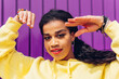 © Dani D.G - African ethnic woman in trendy yellow dress dancing with hands on face against purple background