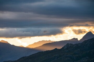 Mountainous landscape with the sun shining under the dense clouds