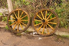 Two Old Wooden Cart Wheels Leaning Against A Wire Fence