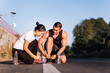 Asian couple tying shoelaces with bottle of water on the road. Runner working out on street. Healthy lifestyle during covid-19 or coronavirus concept.