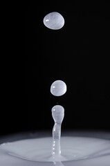 Vertical closeup of waterdrops bouncing above a white liquid against a dark background