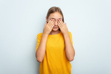 Young caucasian girl isolated on blue background afraid covering eyes with hands.