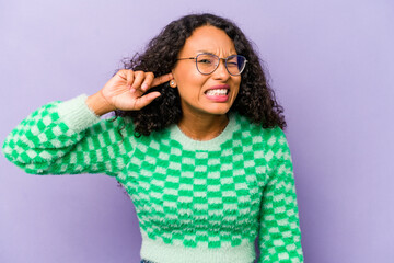 Wall Mural - Young hispanic woman isolated on purple background covering ears with fingers, stressed and desperate by a loudly ambient.