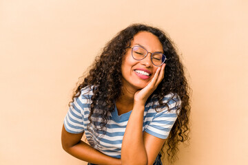 Wall Mural - Young hispanic woman isolated on beige background laughs happily and has fun keeping hands on stomach.