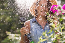 A Girl With A Watering Hose In Close-up. The Farmer's Wife Is Watering The Flowers. The Concept Of Caring For Agricultural Plants And Garden Flowers.