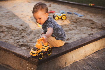 Wall Mural - Boy playing with toys in sandbox. Child having fun on playground in sandpit. Outdoor creative activities for kids. Summer and childhood concept