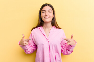 Wall Mural - Young caucasian woman isolated on yellow background person pointing by hand to a shirt copy space, proud and confident