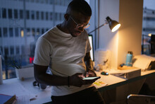 Young Businessman With Smart Phone Working Late In Office