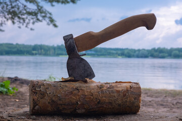 Axe in a log against the background of the river and clouds