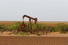 Rusty Oilfield Pump Jack In A Tilled Field At Golden Hour