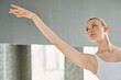 Young graceful ballet dancer with outstretched arm looking forwards during performance on stage or repetition in classroom
