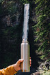 Filling metal flask from waterfall, optical illusion
