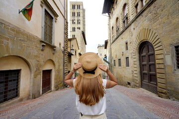 Wall Mural - Beautiful tourist girl holds hat walking in the historic town of Arezzo, Tuscany, Italy