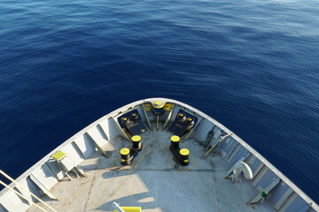 View on calm blue Mediterranean Sea and mooring station with yellow bollards, mooring rollers and panama bow on a forward of cargo container ship from top of mast. There is a copy space.