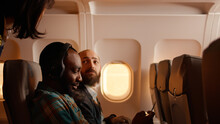 Male Passenger Talking To Flight Attendant On Airplane, Being Seated On Plane And Using Smartphone. Flying During Sunset, Travelling On Vacation Trip With Tourists.