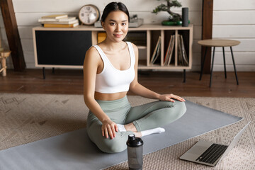 Wall Mural - Young asian woman doing yoga with laptop, listening to meditation instructor on application or website, doing meditating course at home