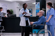 Leinwandbild Motiv African american medic holding clipboard with medical data talking with nurse about senior patient in wheelchair in hospital reception. Older man living with disability in clinic for appointment.