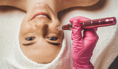 Wall Mural - cosmetologist's hand doing procedure of microneedling to the patient's smiling face. aesthetic cosme