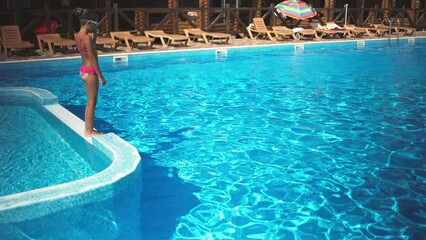 Wall Mural - A girl in a pink swimsuit with swimming goggles jumps into a pool of blue water and creates splashes around