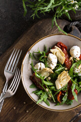 Wall Mural - bowl with salad with mozzarella, arugula, artichokes and sun-dried tomatoes on the table