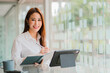 © ArLawKa - Beautiful smiling Asian businesswoman working using a tablet at the office while sitting in a modern office successful business idea