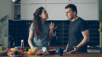 Pretty woman standing at table cutting salad while her boyfriend comes and they argueing speaking loud and nervous. Relations , difficulties concept