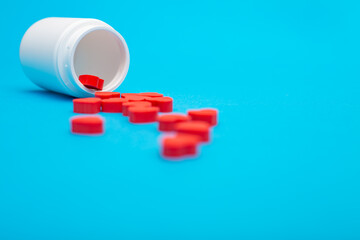 Red heart shaped pills with plastic bottle on blue background.Concept love addiction, love drugs, Valentine's Day and depression