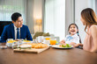 Asian family father, mother with children daughter eating breakfast food on dining table kitchen in mornings together at home before father left for work, happy couple family