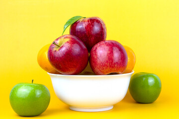 Poster - Set of Healthy fruits in a white bowl, green apples, red apples, oranges isolated on yellow background. Close up composition of colorful of fruits isolated on yellow background