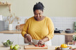 © Seventyfour - Waist up portrait of smiling black woman cooking healthy meal in kitchen and cutting vegetables, copy space